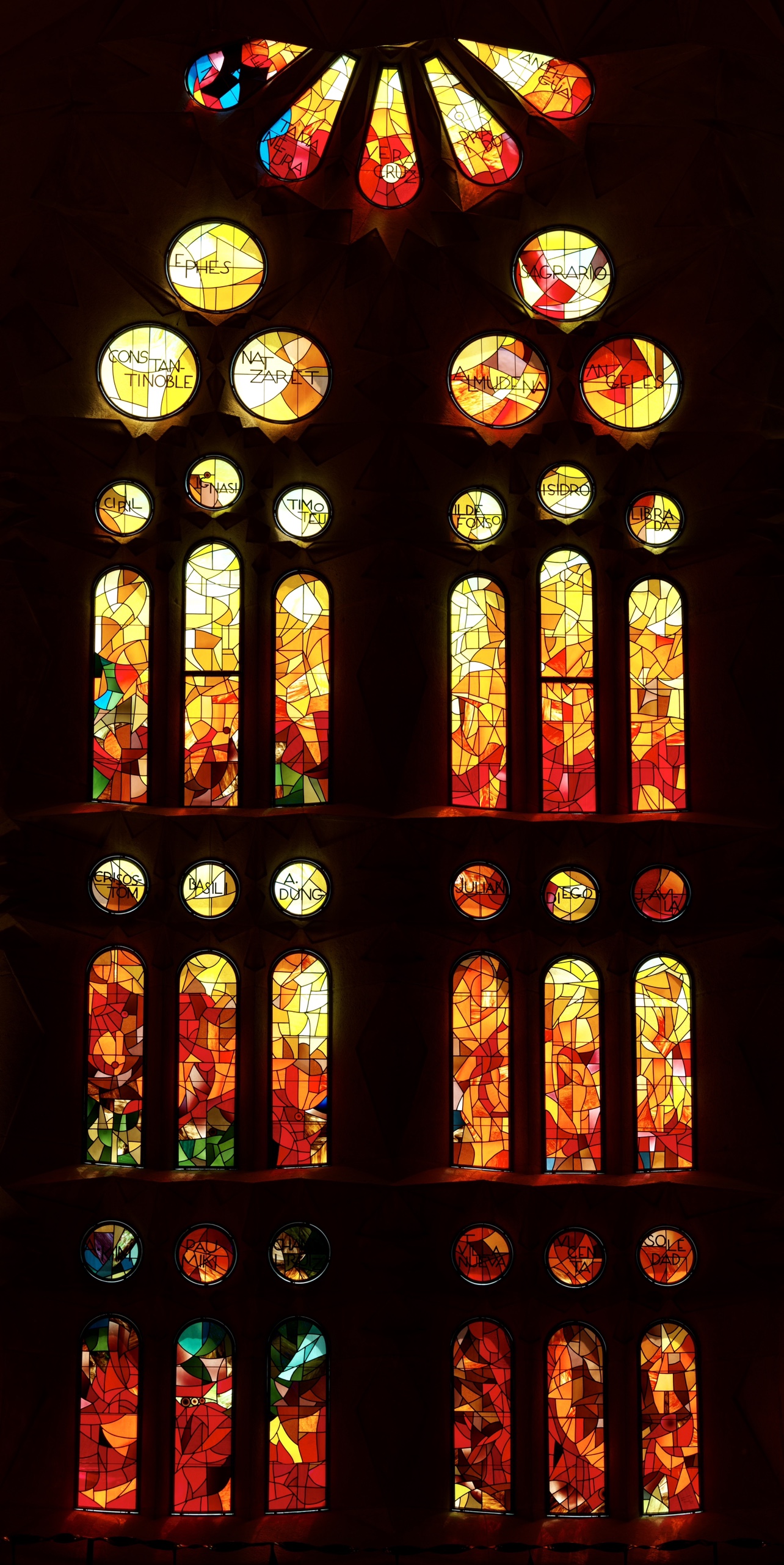 Vertical Sagrada Família glass — someone, vermilion and blue stacked in dark stone.